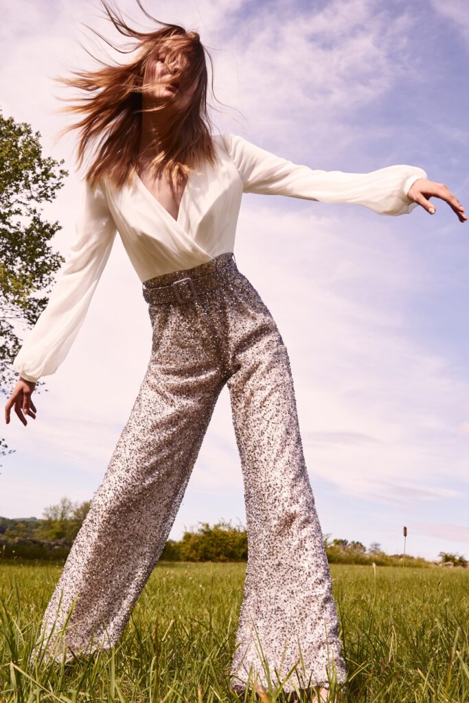 A relaxed white silk blouse with long sleeves paired with wide-leg silver sequin pants.