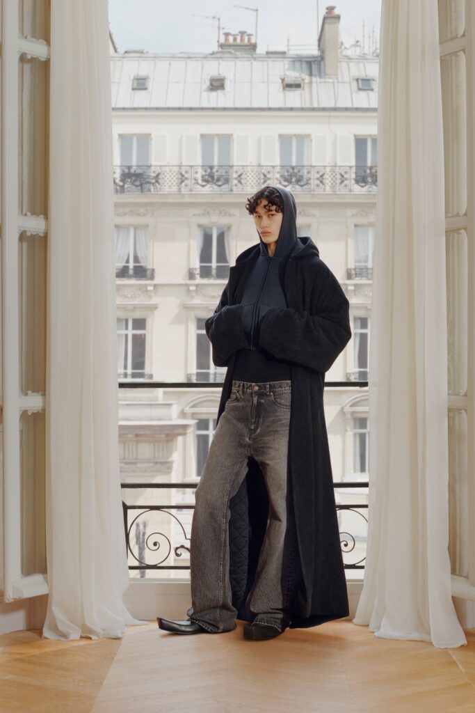 A relaxed black coat layered over a gray hooded sweatshirt, paired with denim pants.