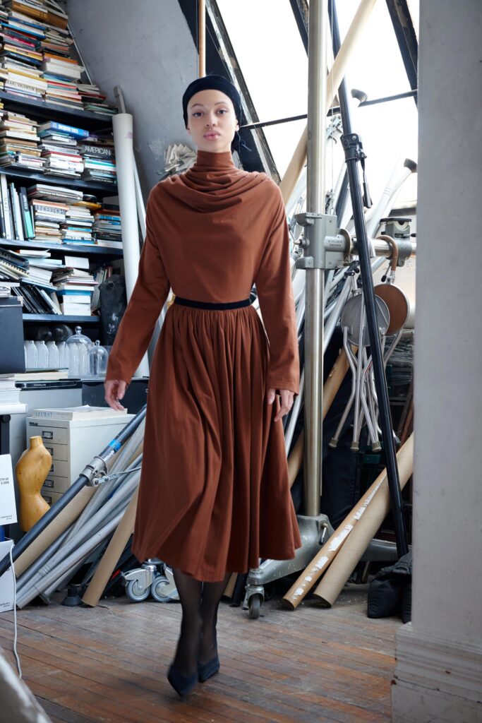 A fitted brown cotton long-sleeve dress with a high neckline and pleated design.