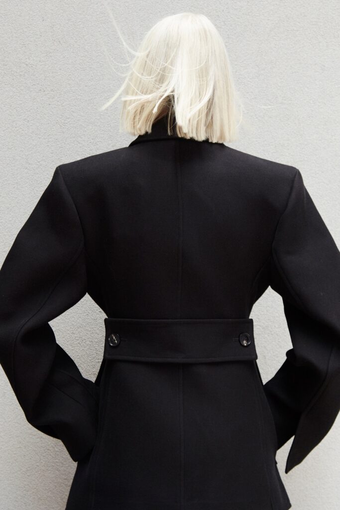 A structured black wool coat with long sleeves and a collared design featuring button details.