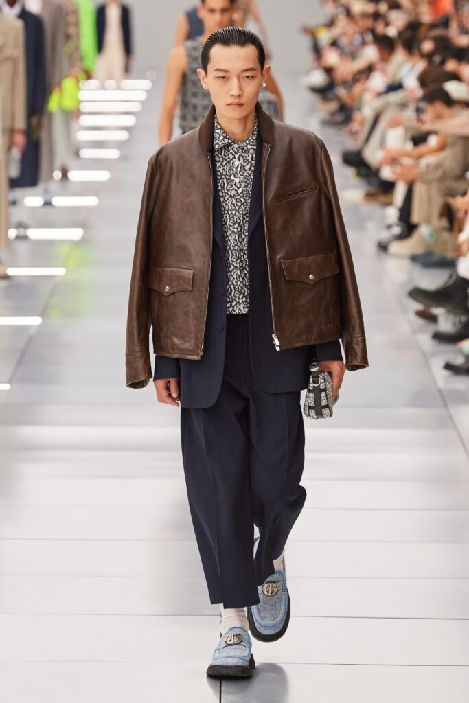 A relaxed brown leather jacket paired with navy cotton pants, featuring a collared design.