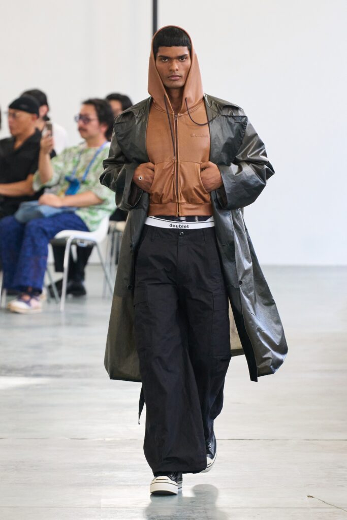 A relaxed black leather coat layered over a brown hooded sweatshirt.
