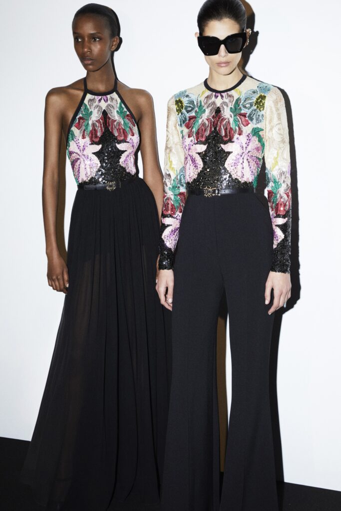 A fitted black jumpsuit with a multicolor floral design and long sleeves, featuring a V-neckline.