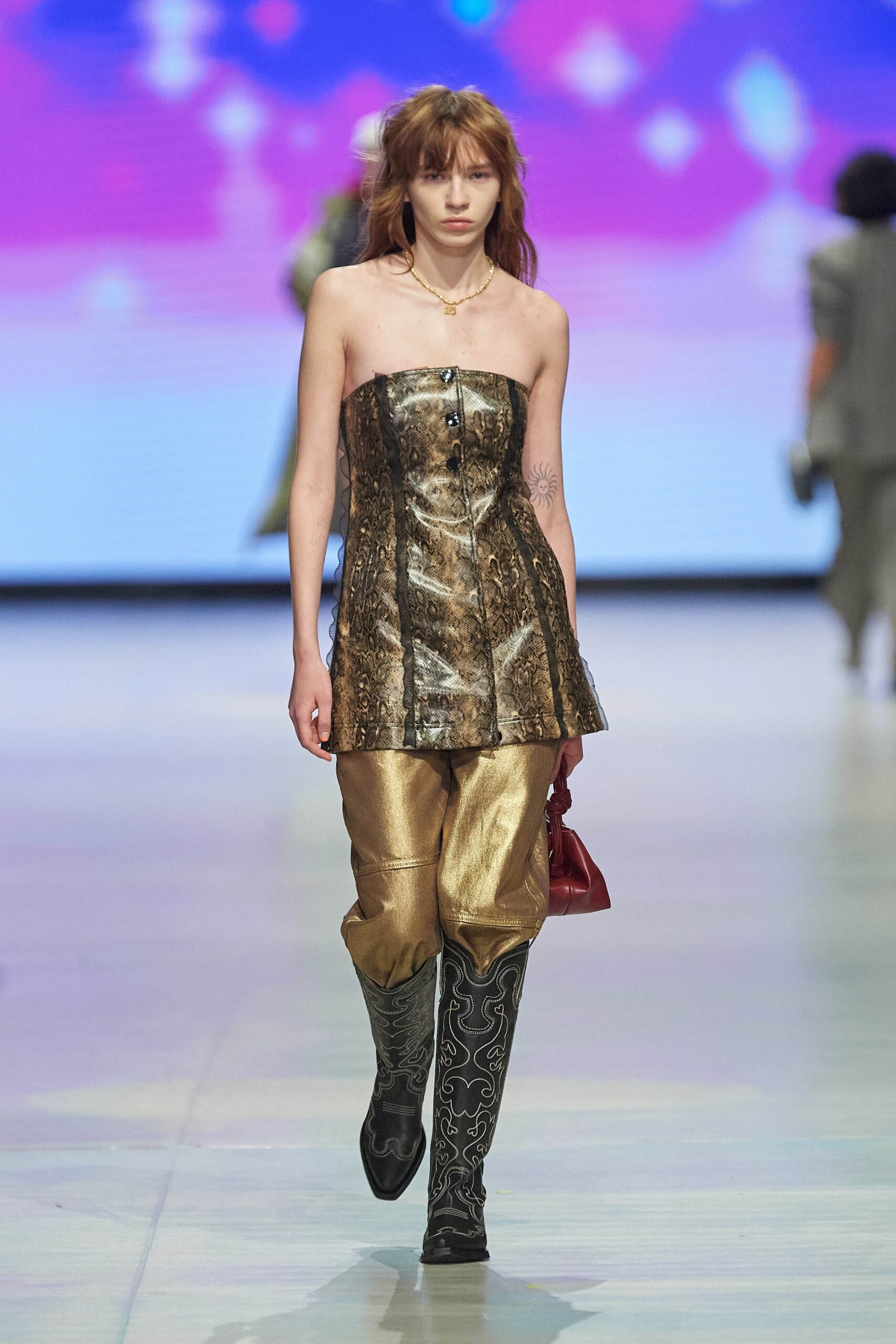 A fitted sleeveless gold silk top with a V-neck and asymmetric design paired with black pants.
