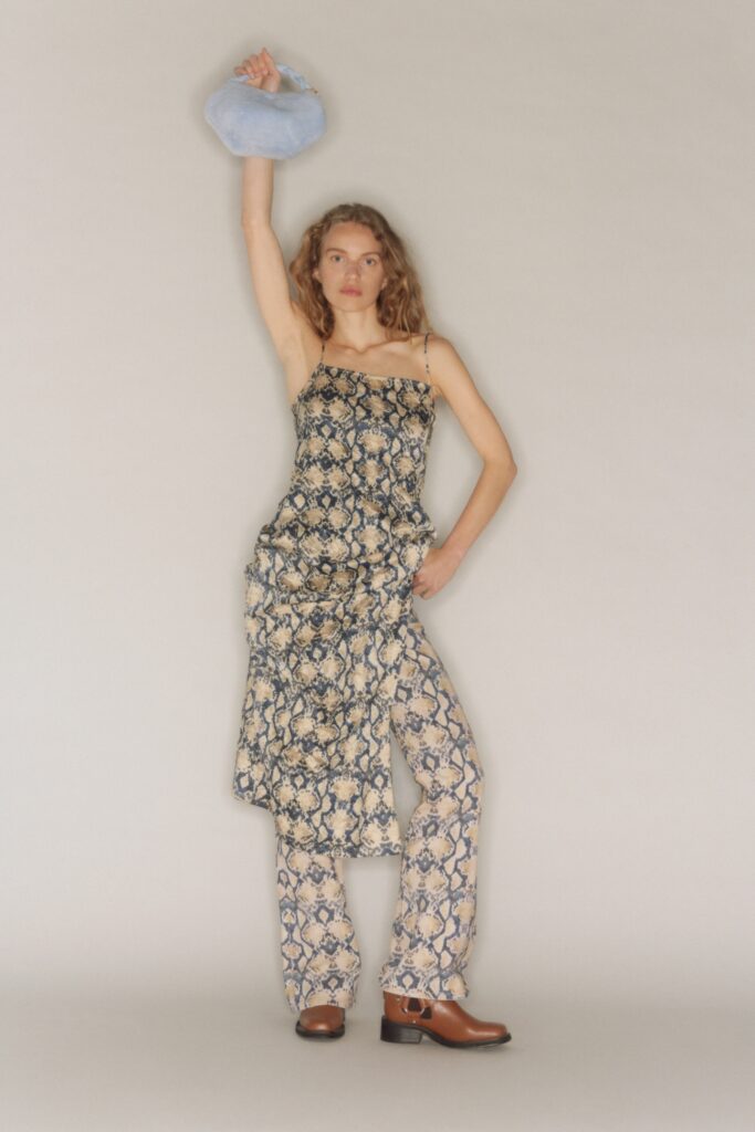A relaxed fit beige printed sleeveless dress paired with flared pants.