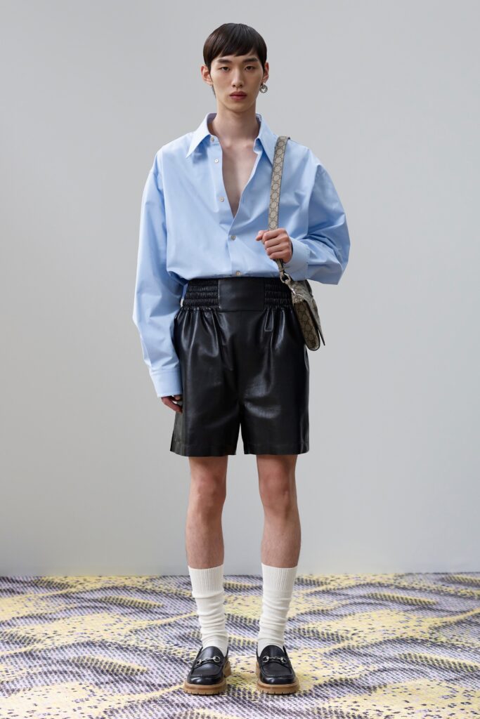 A relaxed blue cotton long-sleeve shirt paired with pleated black leather shorts.