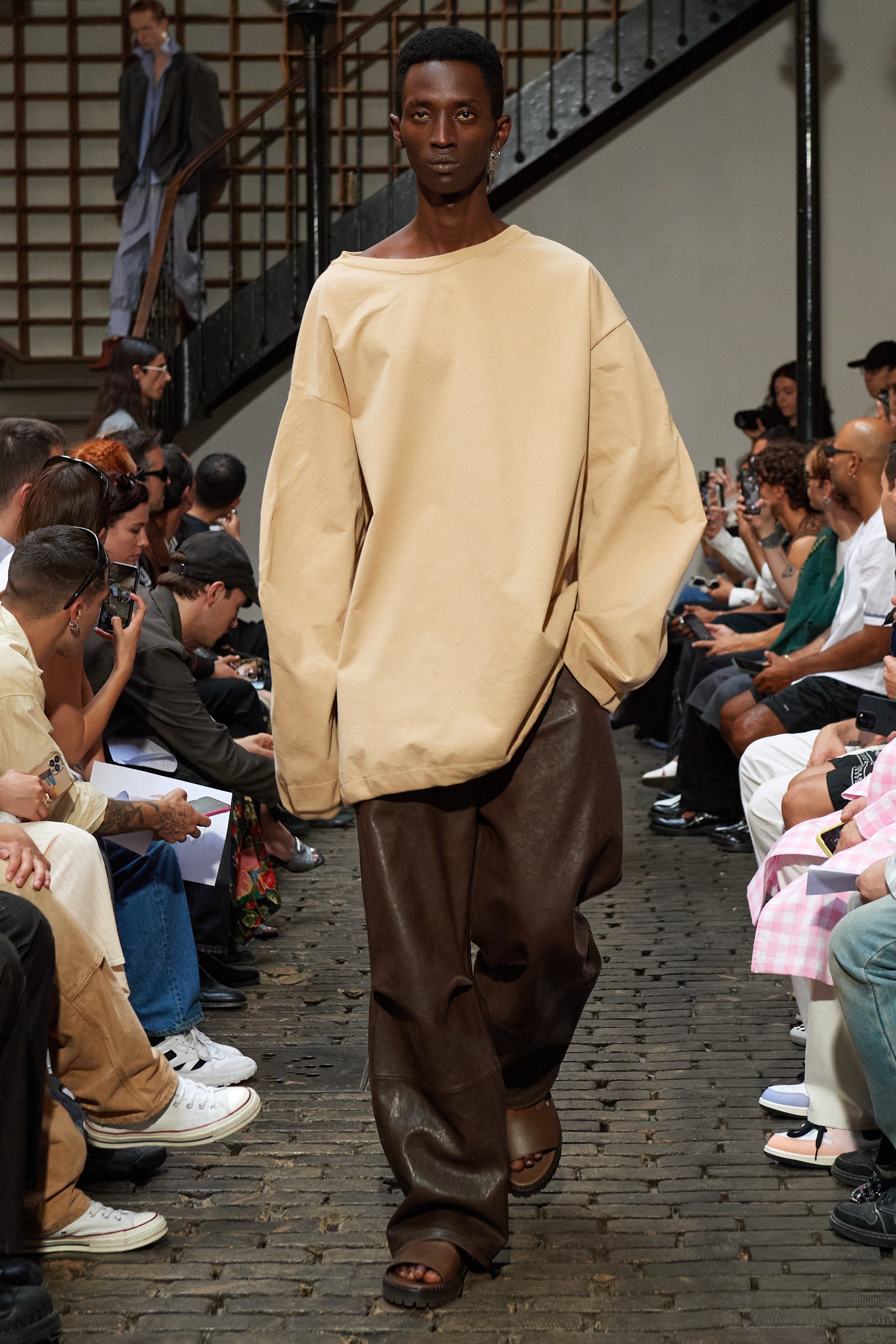 An oversized beige top paired with brown leather pants, creating a relaxed and stylish look.