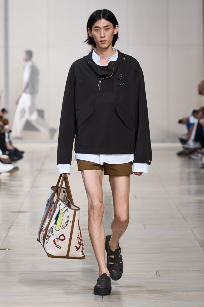 A relaxed black jacket with a collared neckline paired with brown shorts.