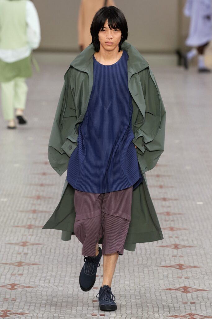 A relaxed green coat layered over a blue pleated top, featuring a collared design.