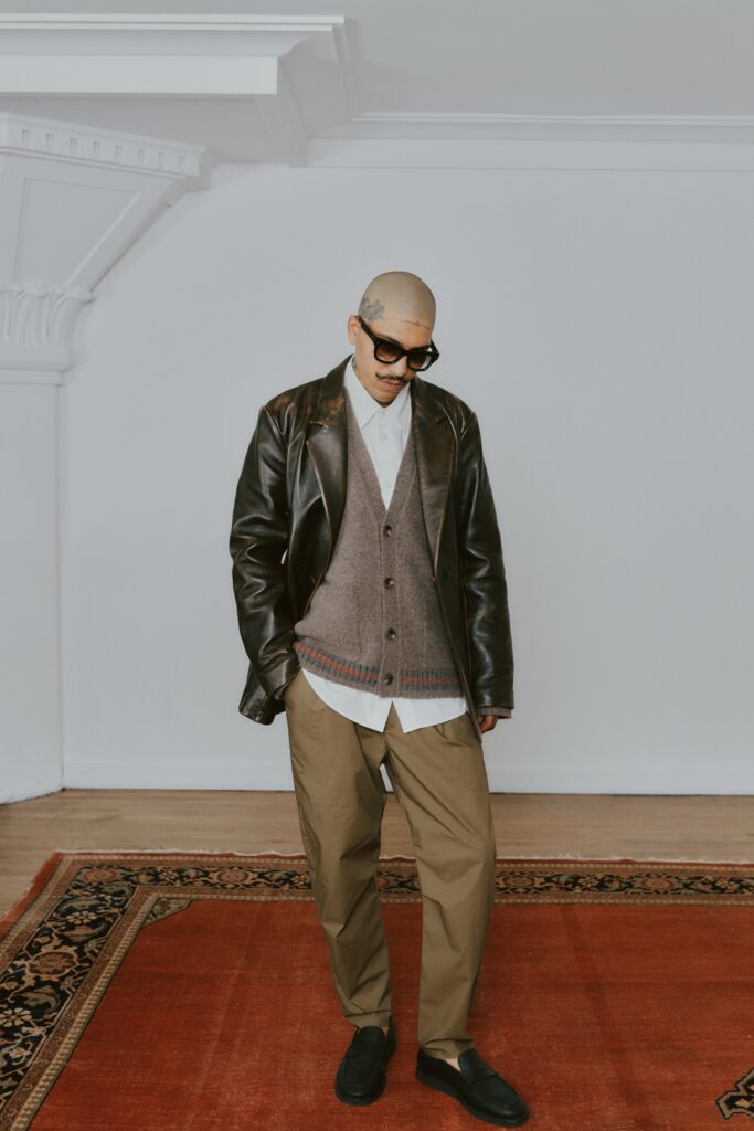 A relaxed black leather jacket layered over a gray wool vest with a collared shirt.