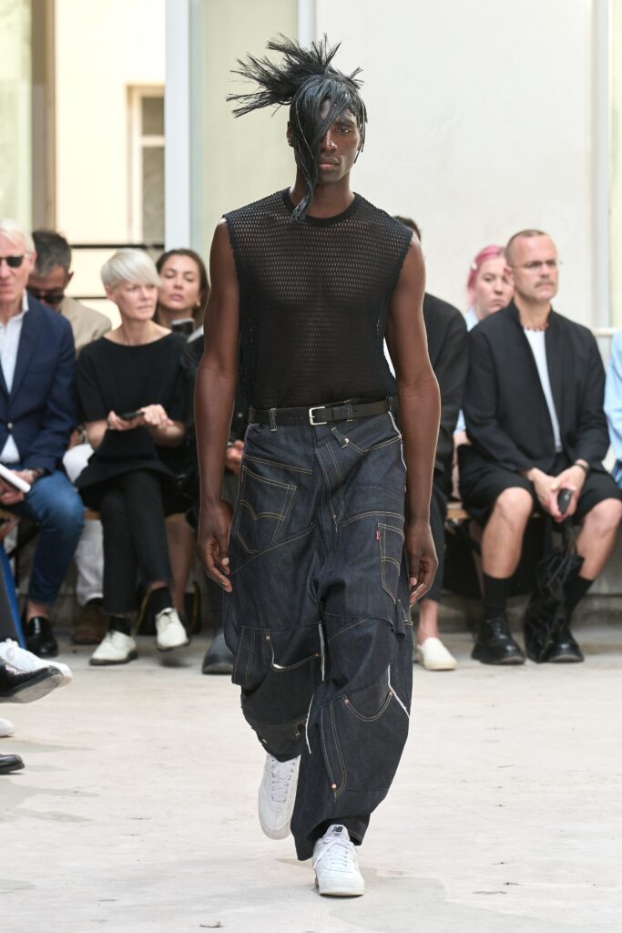 A relaxed black sleeveless top paired with layered blue denim pants.