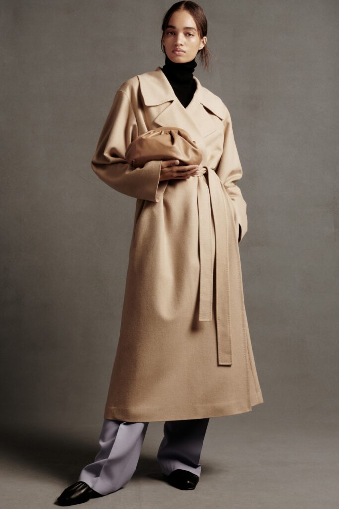 A relaxed beige wool coat with a belted waist and long sleeves, paired with lavender pants.