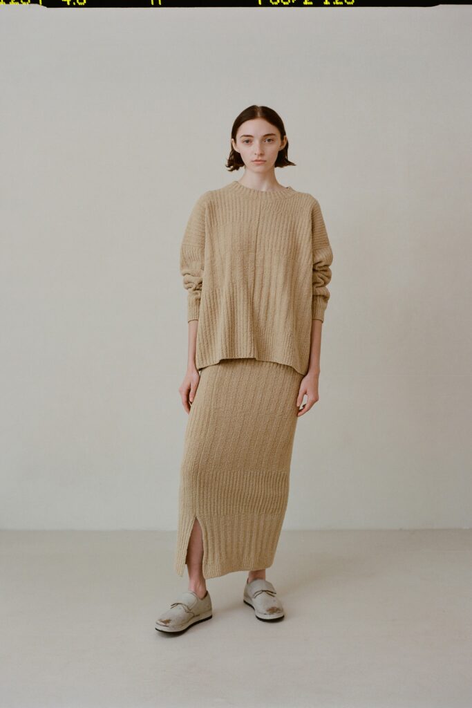 A relaxed beige knit long-sleeve top paired with a matching skirt featuring a slit.
