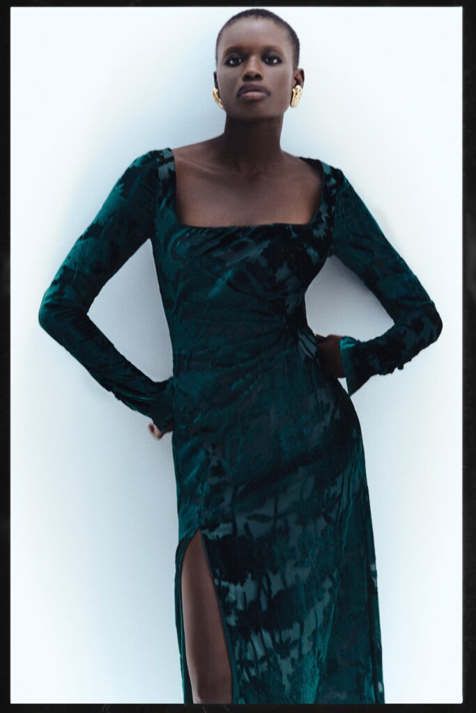A fitted green velvet dress with long sleeves and a square neckline featuring a stylish slit.