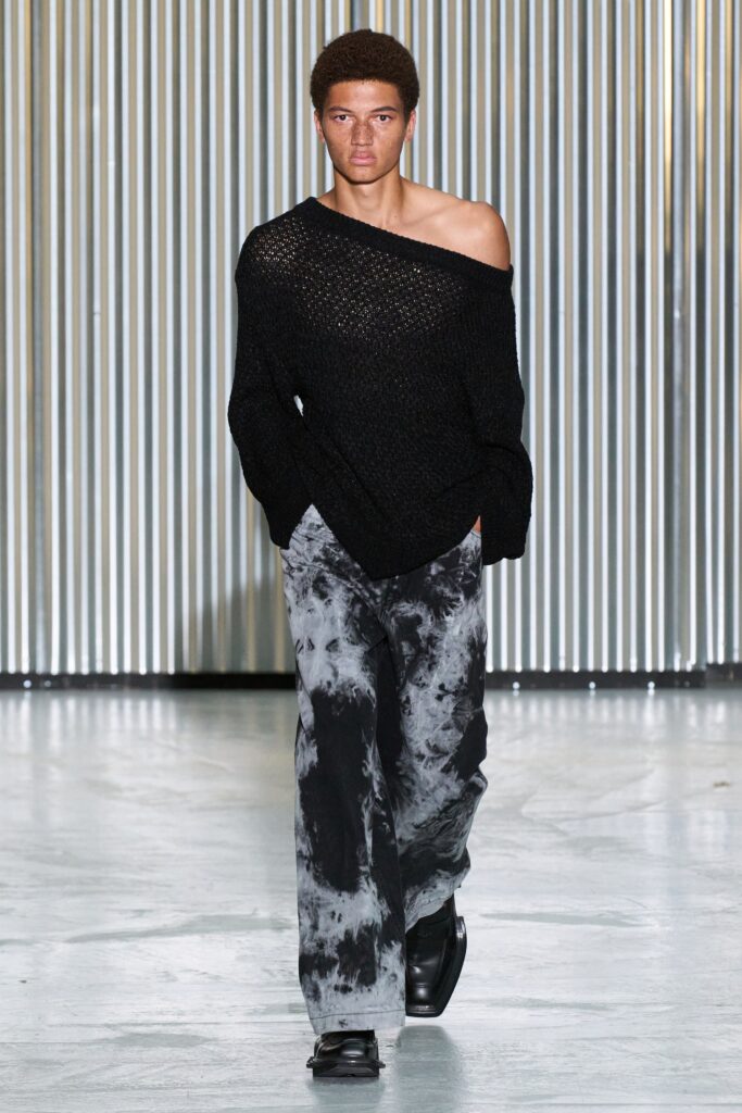 A relaxed black off-shoulder sweater paired with gray printed wide-leg pants.
