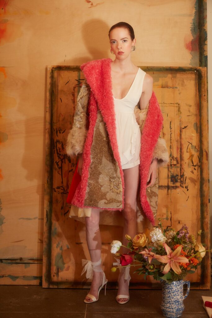 A fitted pink fur coat layered over a silk v-neck dress with embroidered details.
