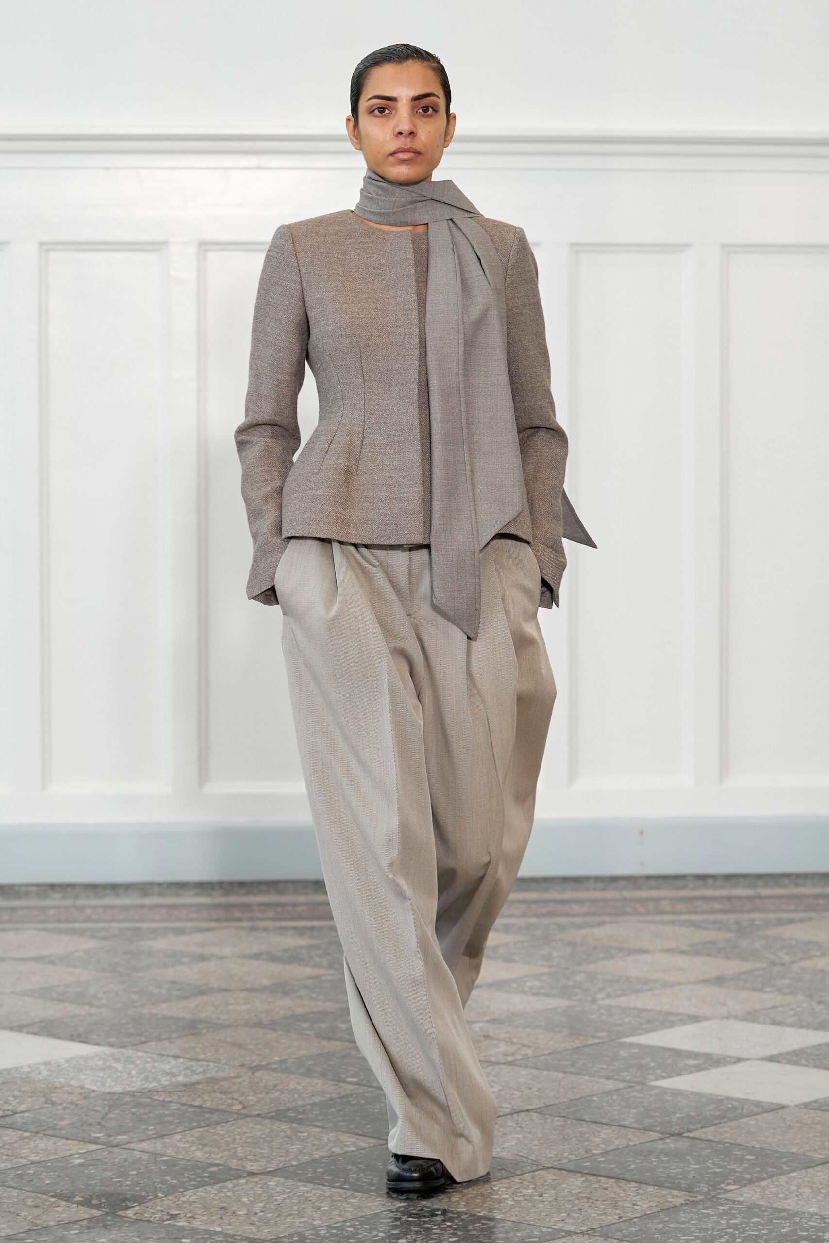 A tailored beige blazer with a collar and long sleeves, paired with gray pants featuring an asymmetric design.