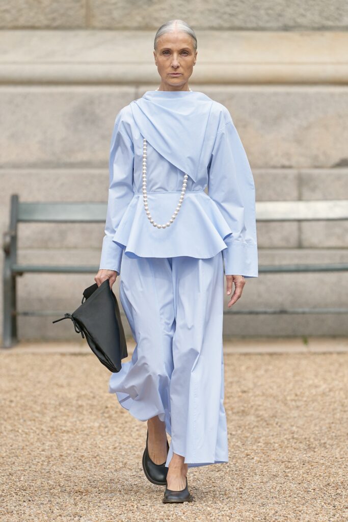 A relaxed blue cotton dress with long sleeves, high neckline, and pleated design details.