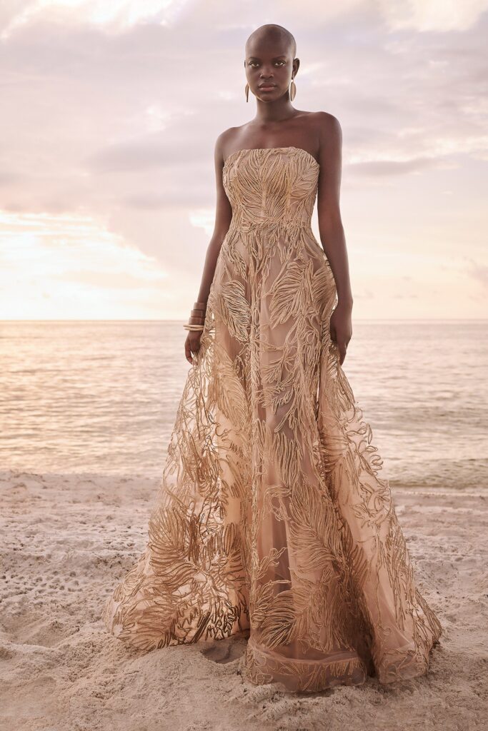 A fitted beige silk strapless gown with intricate embroidery and a flowing maxi silhouette.