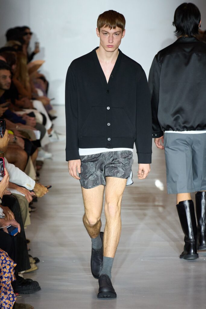 A relaxed black jacket with a collared neckline paired with printed gray shorts.