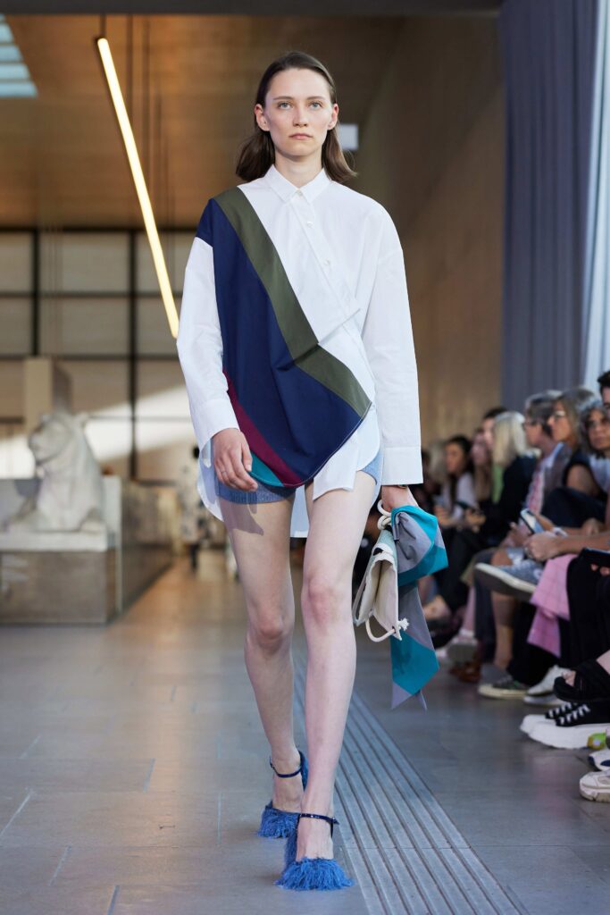 An asymmetric white cotton shirt-dress with long sleeves and a colorful draped detail.