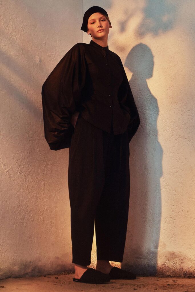 A relaxed black long-sleeve collared top paired with black pants featuring an asymmetric design.