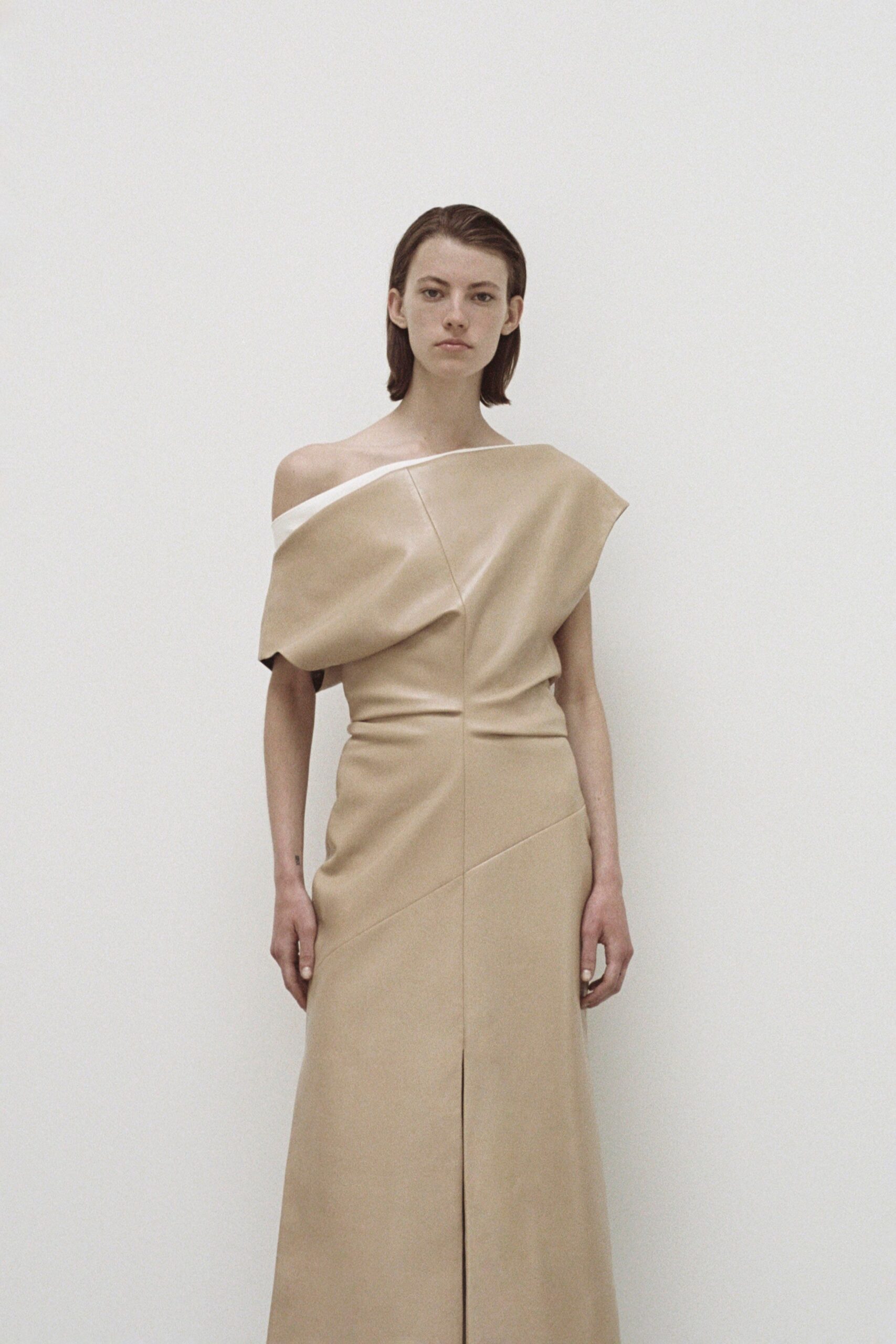 A fitted beige leather off-shoulder dress with an asymmetric design detail.