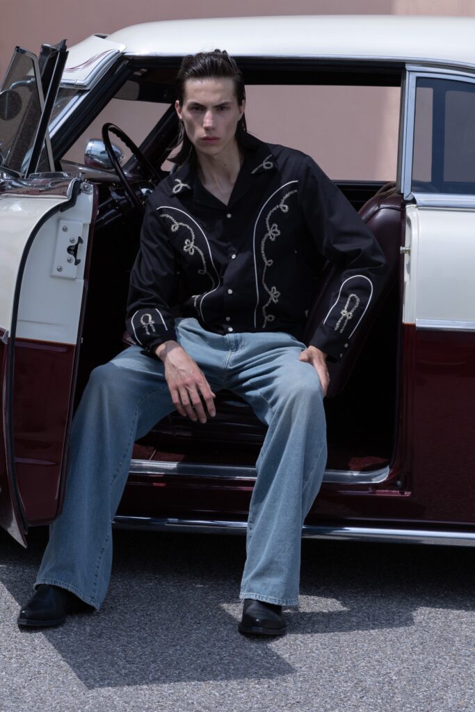 A relaxed black long-sleeve embroidered shirt paired with wide-leg blue denim pants.