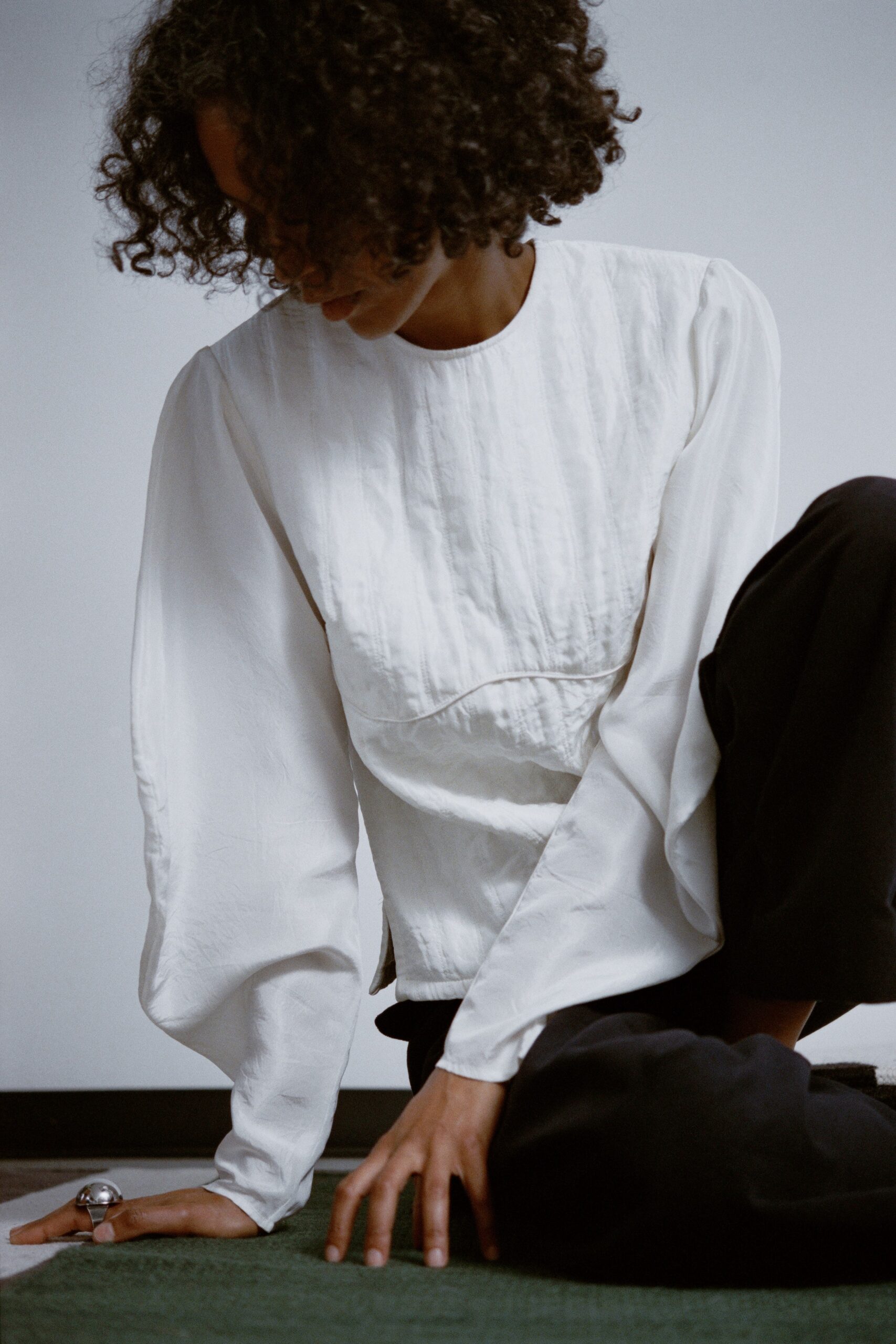 A relaxed white blouse with long sleeves and pleated detail, paired with black pants.