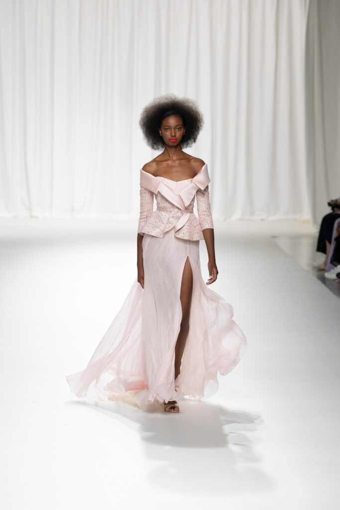 A fitted pink silk off-shoulder dress with a slit and layered design.