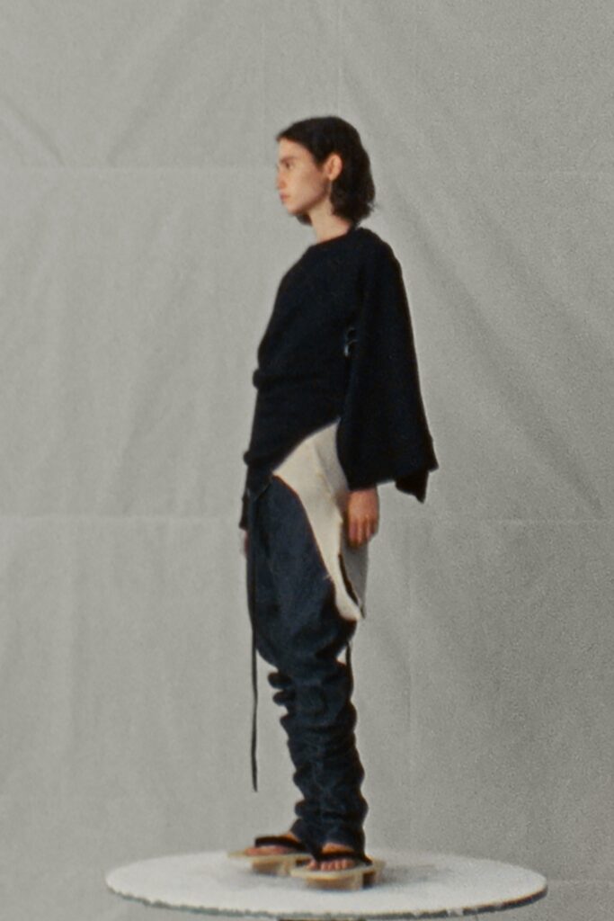 A relaxed black long-sleeve top paired with beige layered pants featuring an asymmetric design.