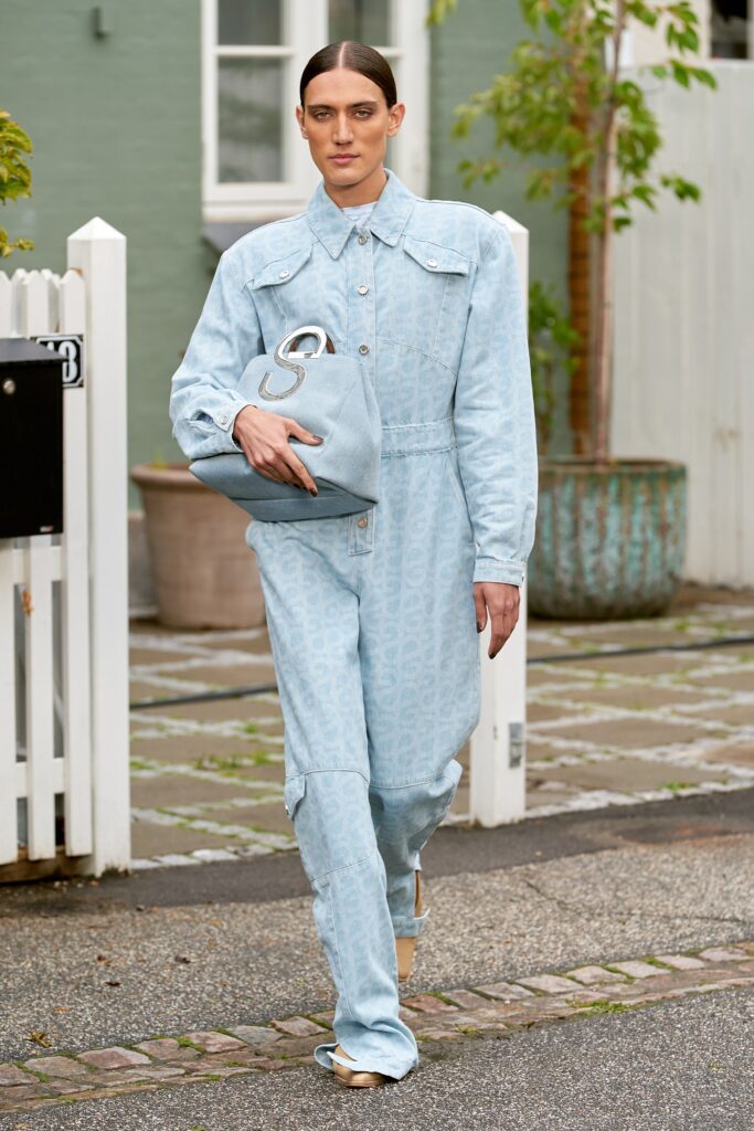 A fitted blue denim jumpsuit with long sleeves, a collared neckline, and a printed design.