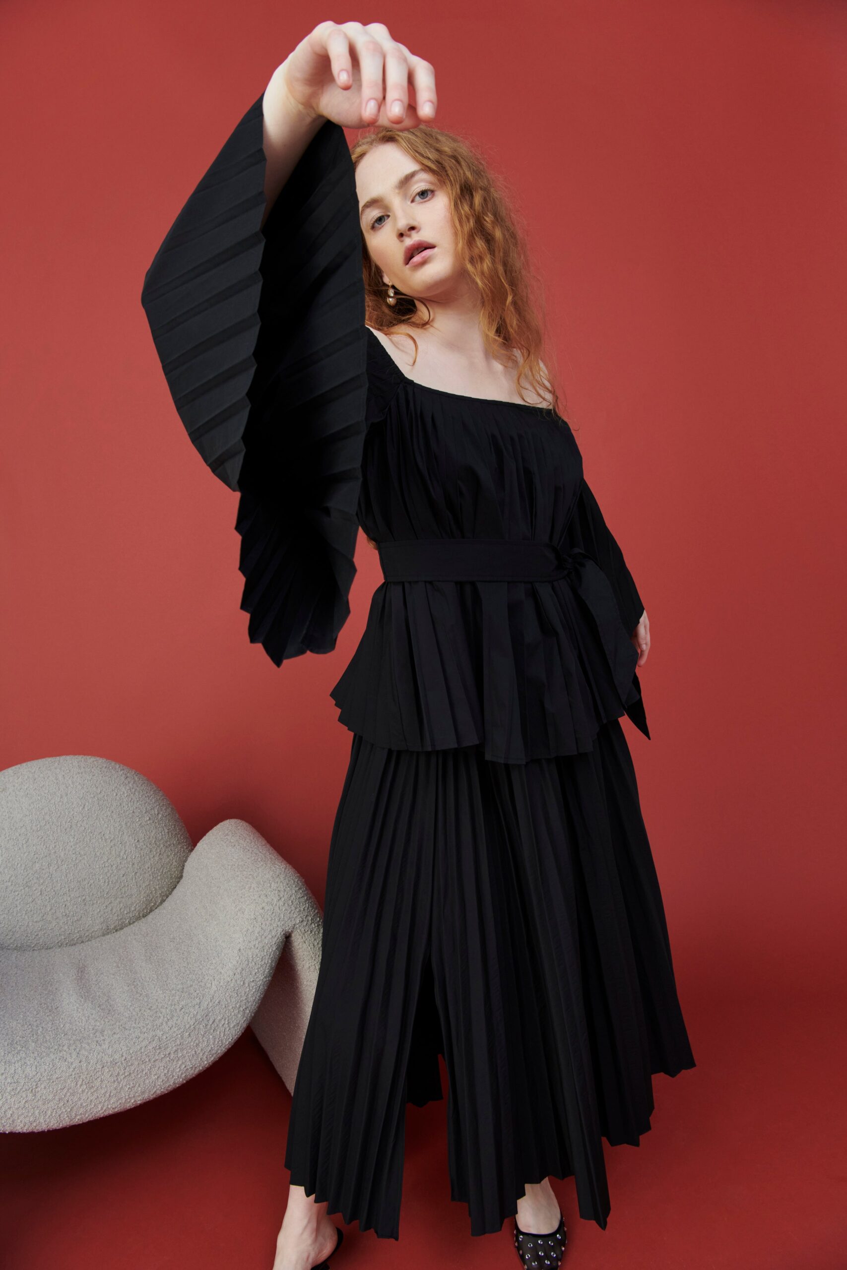 A relaxed black dress with pleated details and an off-shoulder long-sleeve design.