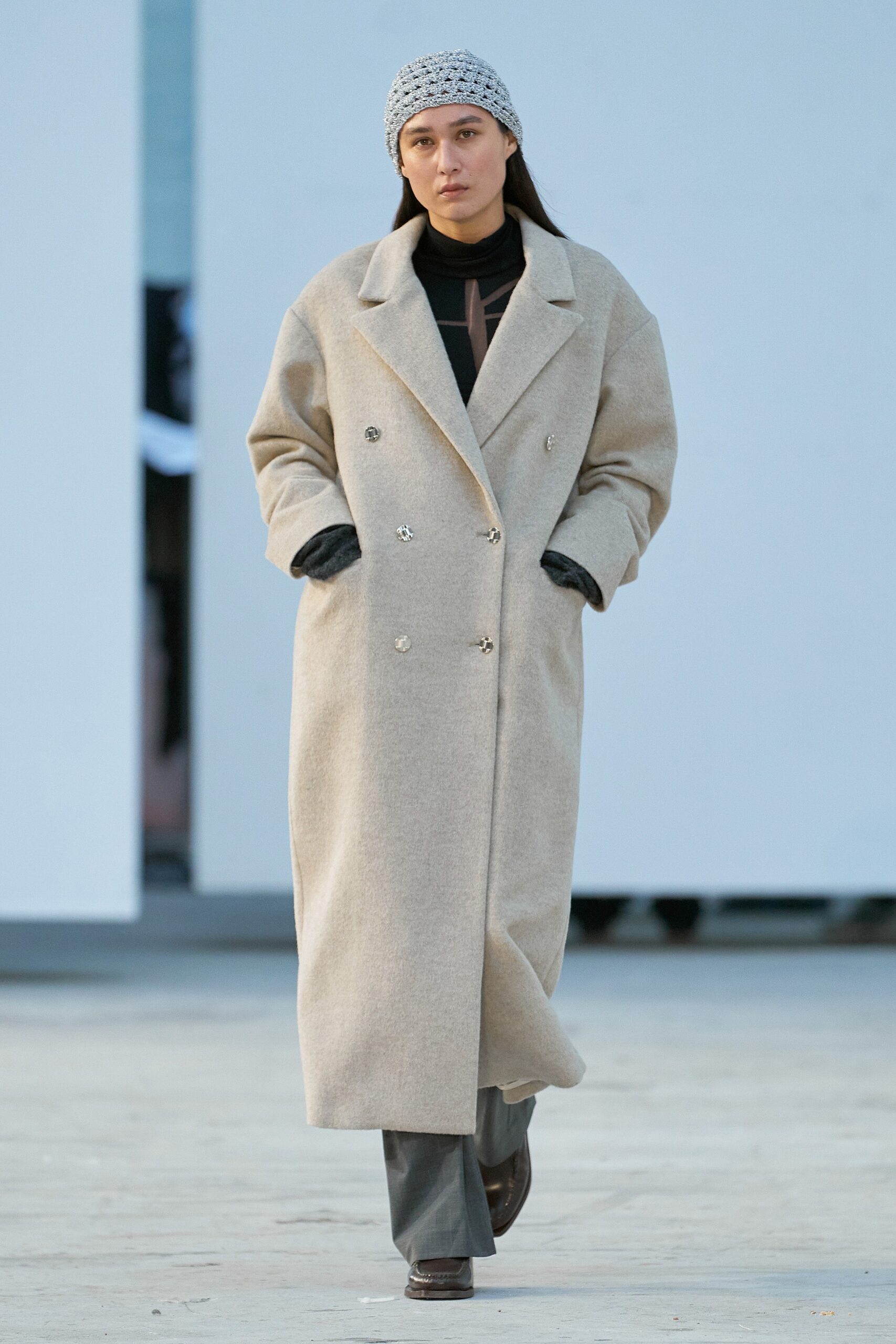 A relaxed-fit beige wool coat paired with gray pants, featuring a collared design and buttoned details.