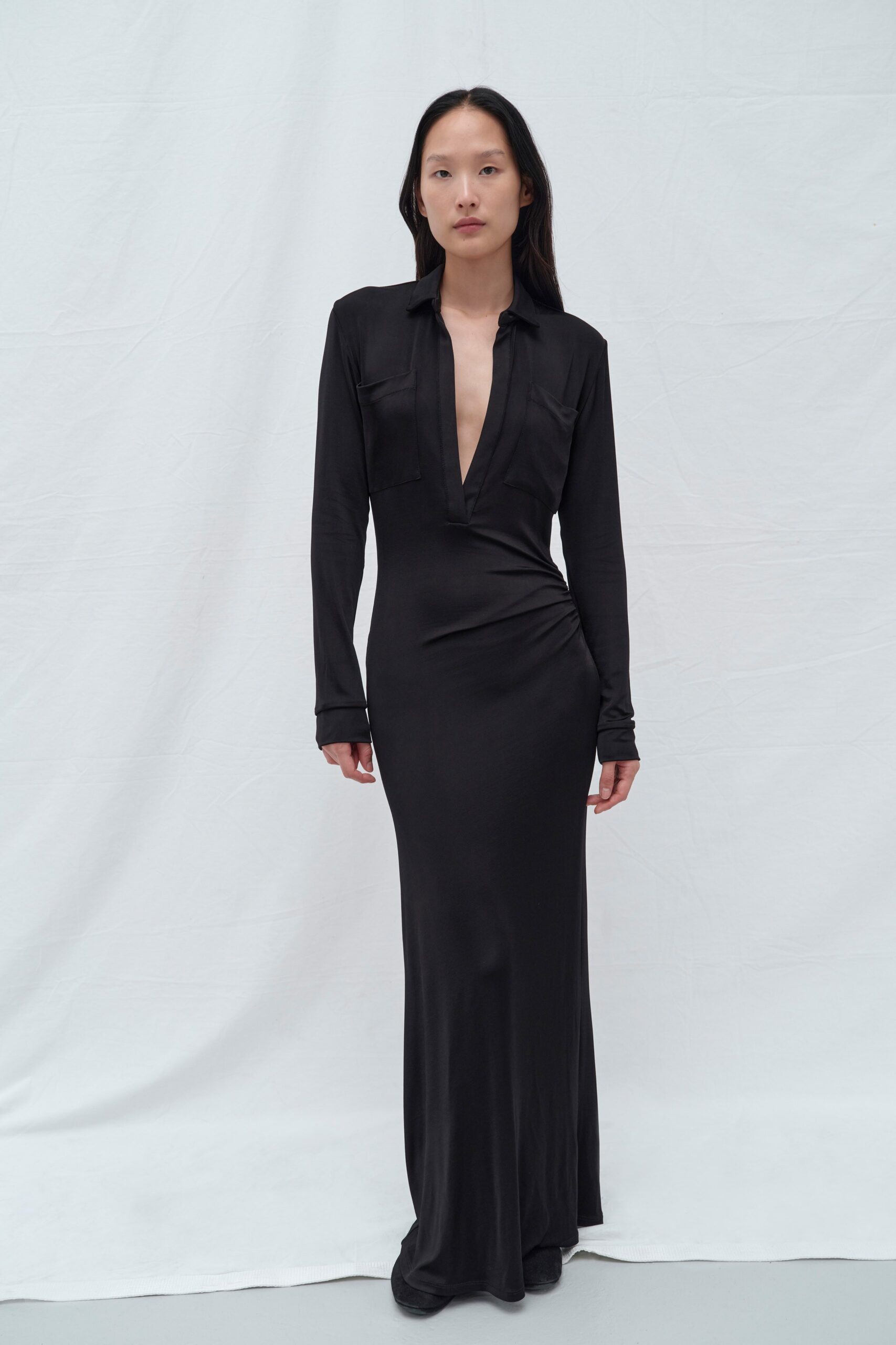 A fitted black silk dress with long sleeves and a V-neckline featuring a stylish slit.