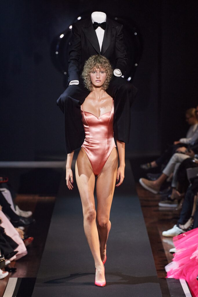 A fitted pink satin swimsuit paired with a black jacket, featuring a sleeveless design and asymmetric detail.