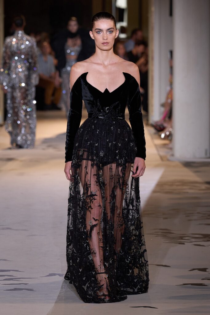 A fitted black velvet sleeveless dress with a V-neckline and tiered design.