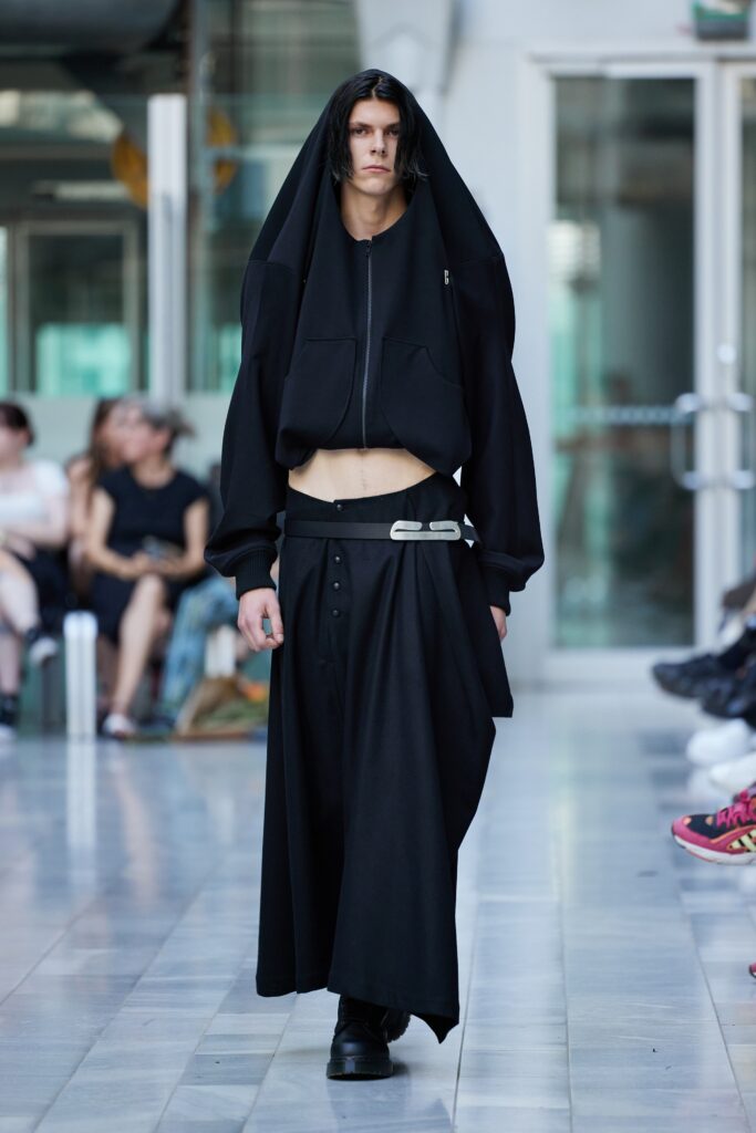 An oversized black hoodie paired with an asymmetric black skirt for a bold runway look.