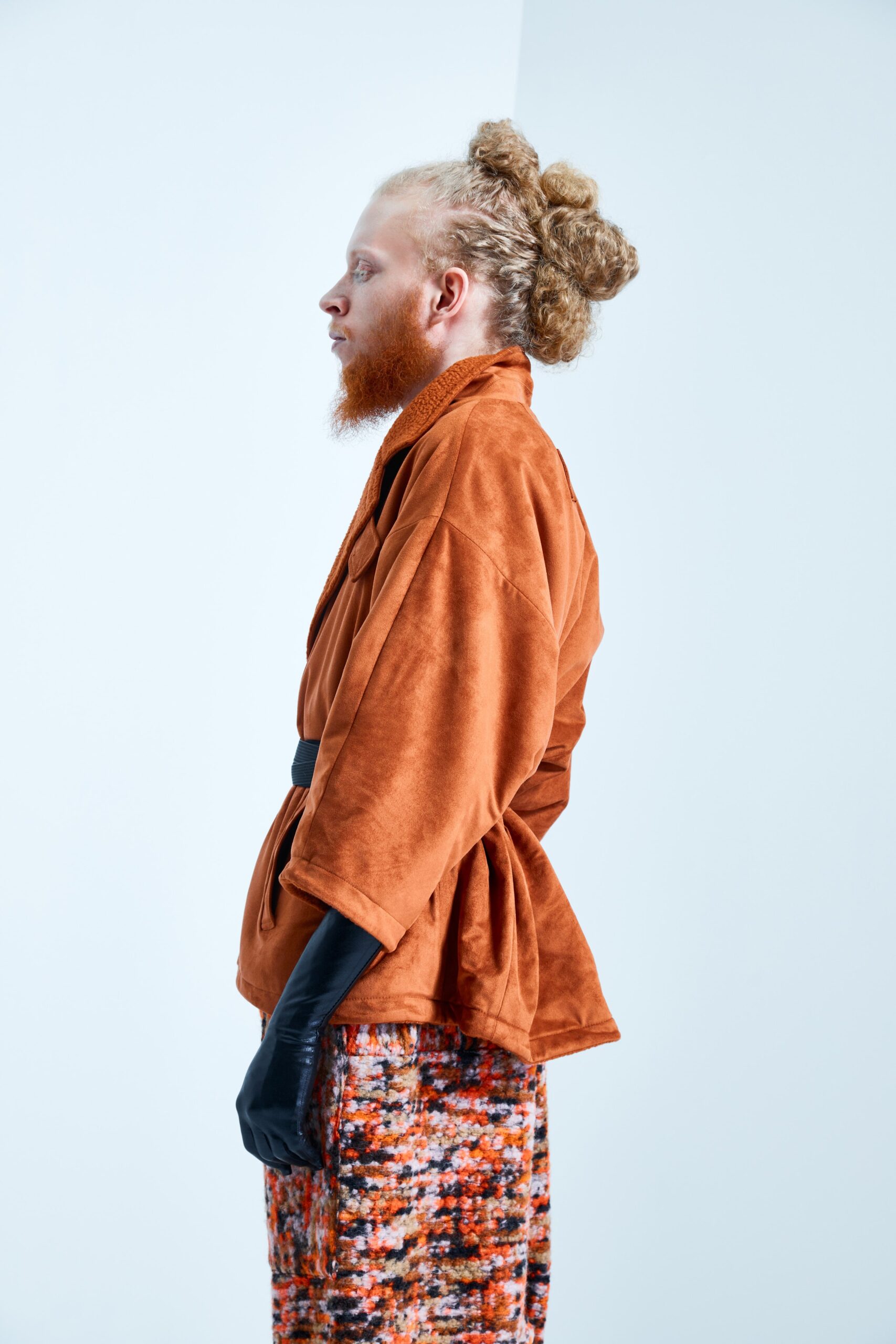 This relaxed jacket in a rich orange suede features a collared design and long sleeves, creating a soft yet structured silhouette. Paired with a multi-colored printed skirt, the ensemble showcases a dynamic interplay of textures and patterns, enhancing the visual narrative.