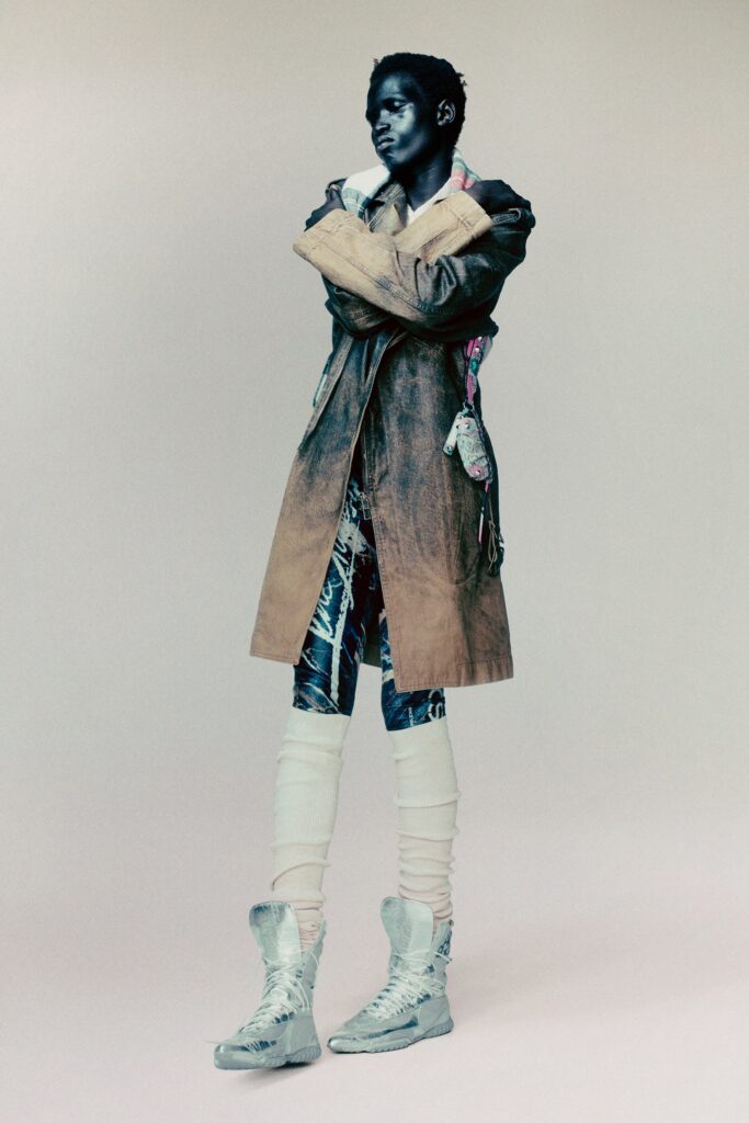 A fitted beige coat paired with black denim pants featuring an asymmetric design.