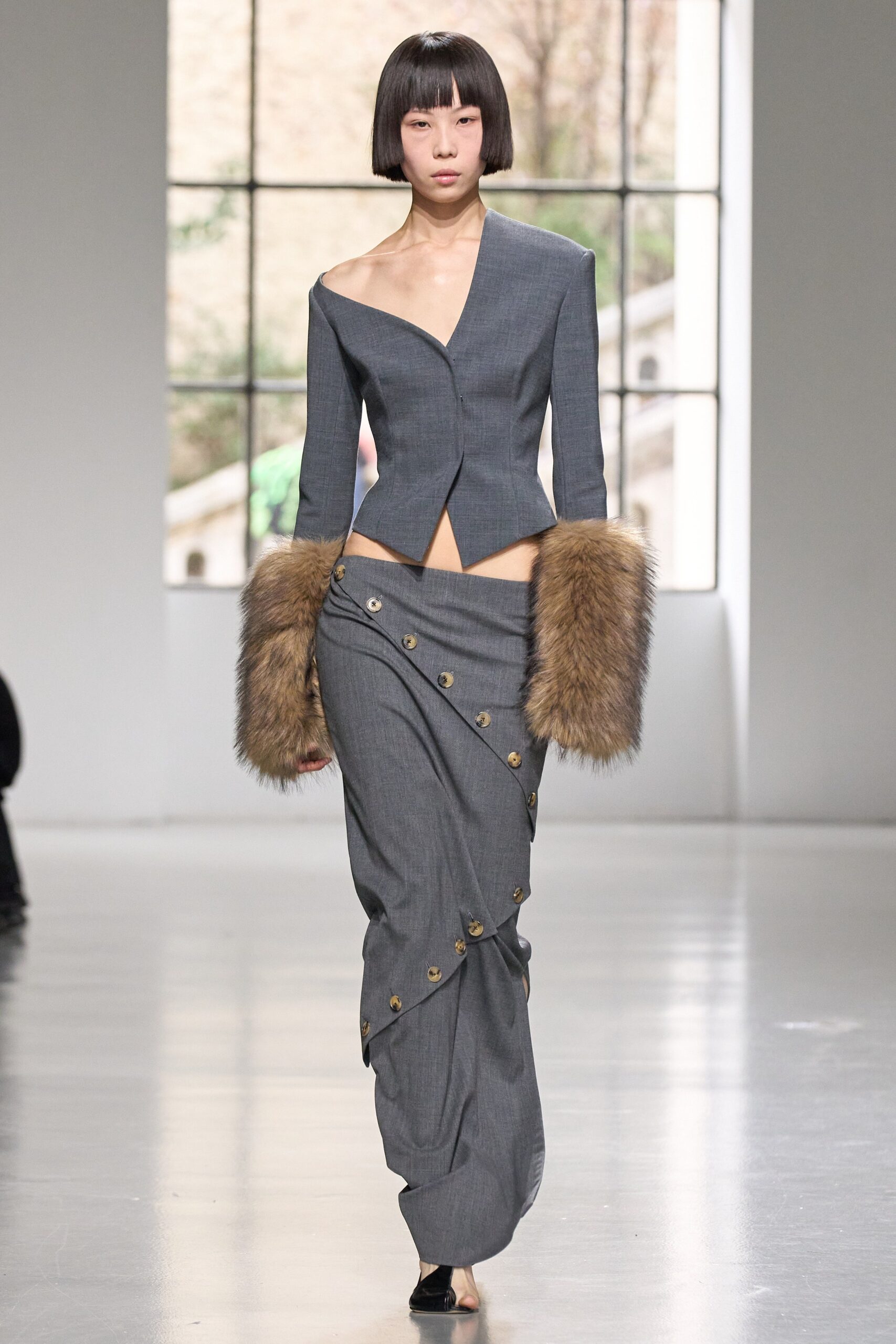 A fitted gray wool blazer with an off-shoulder design paired with a buttoned asymmetric skirt.