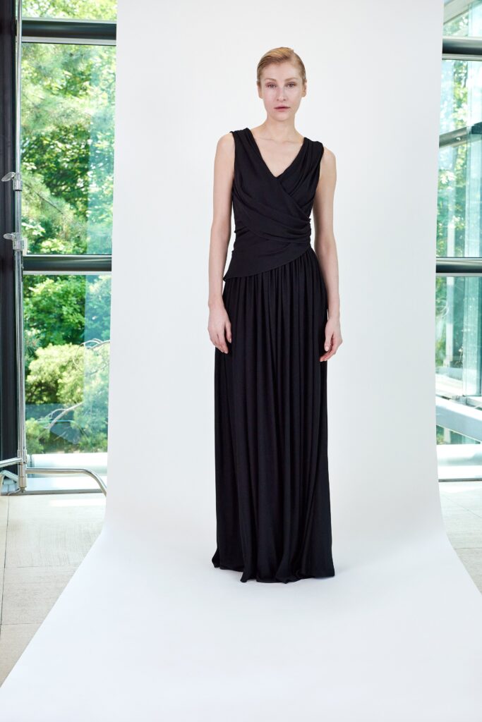 A fitted black sleeveless dress with a V-neckline and draped design.