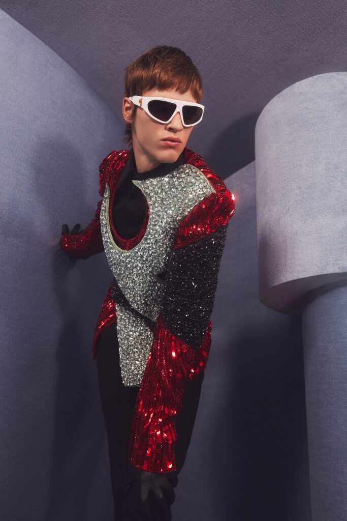 An asymmetric red sequined jacket paired with black pants, featuring long sleeves and a bold design.