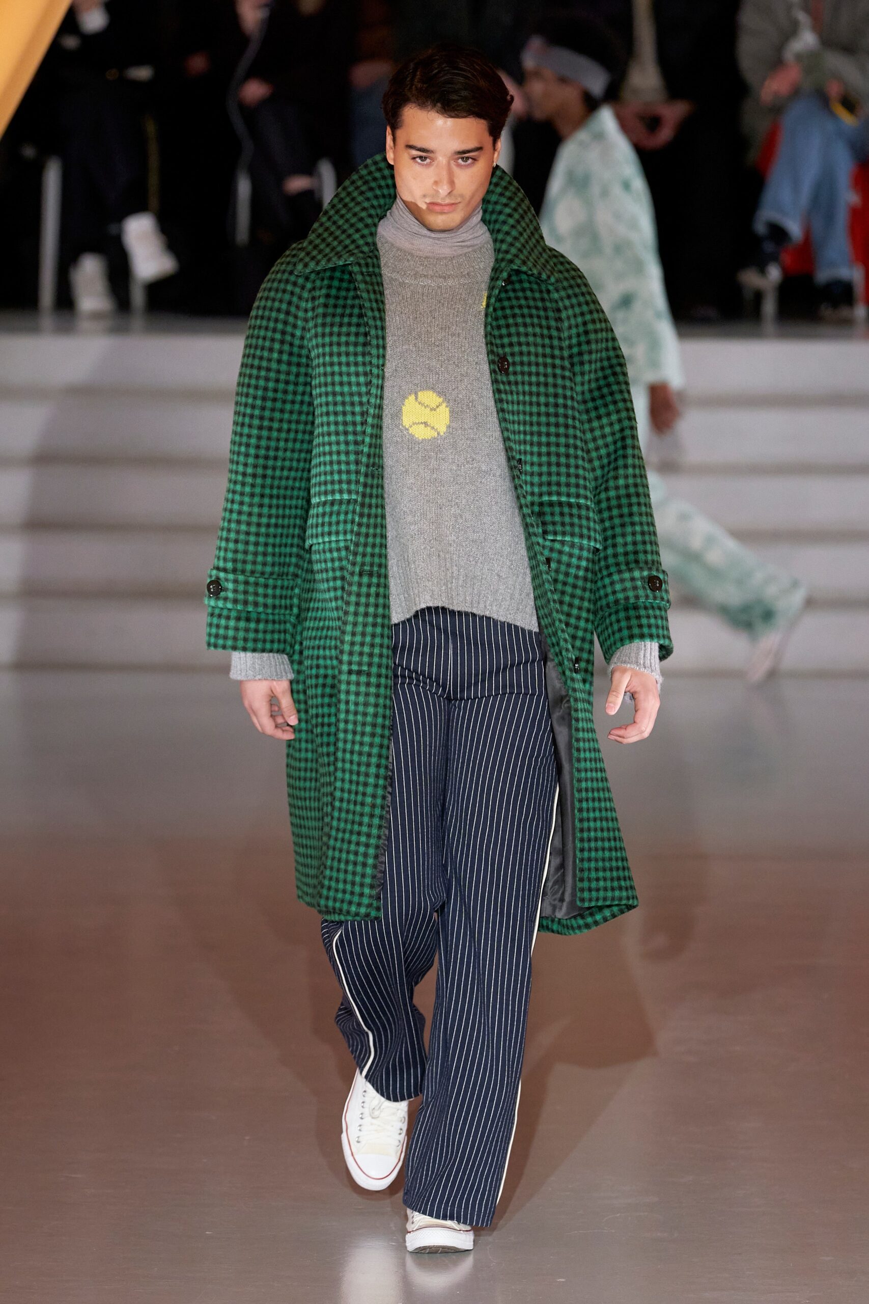 A relaxed green checked coat layered over a gray sweater with navy striped pants.