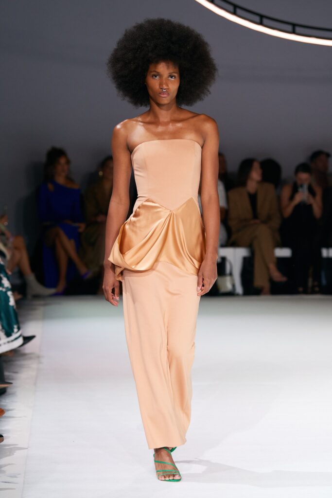A fitted beige silk strapless dress with a draped design detail.