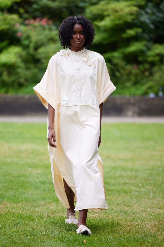 An asymmetric cream cotton dress with a cape detail and long sleeves, perfect for a stylish look.