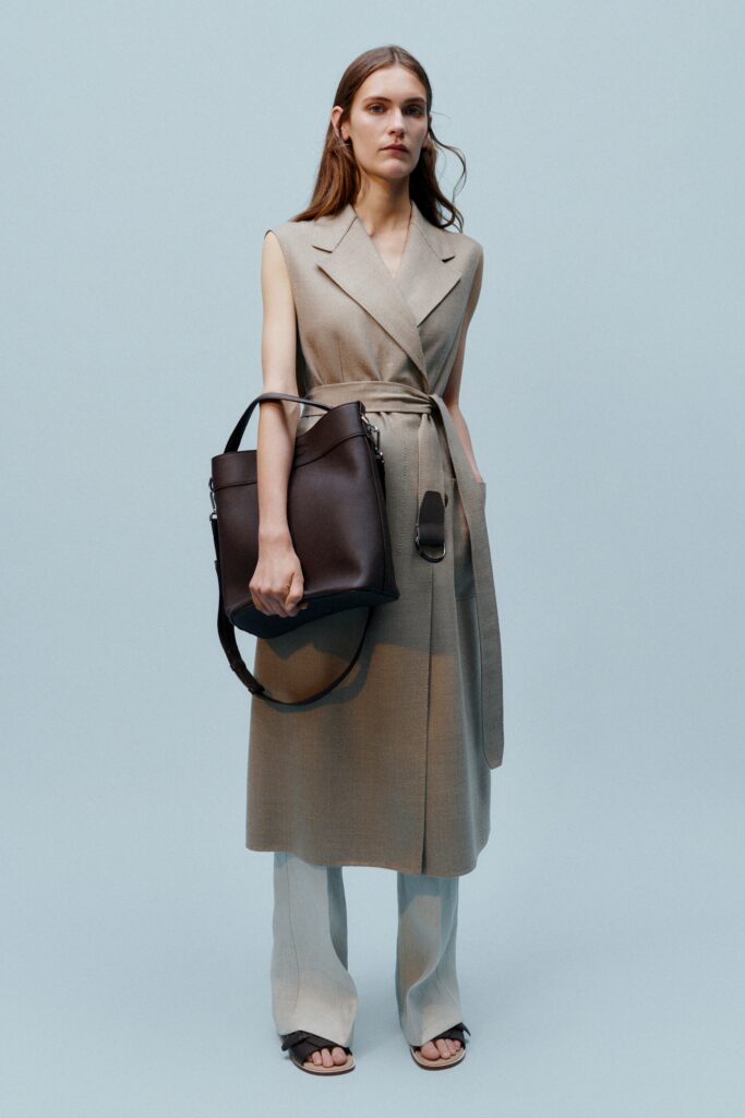 A fitted beige sleeveless belted dress paired with straight-leg pants.