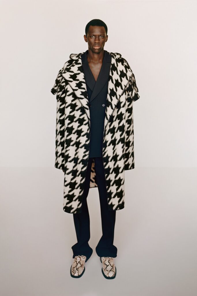 A relaxed black and white checked coat worn over a suit with a collared design.