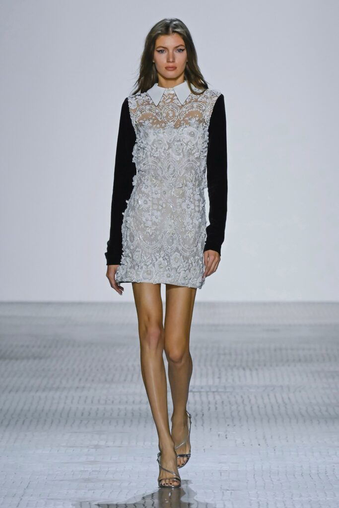 A fitted black and white embroidered dress with long sleeves and a collared neckline.