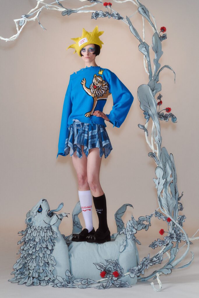 A fitted blue cotton long-sleeve top with an asymmetric design paired with a pleated plaid skirt.